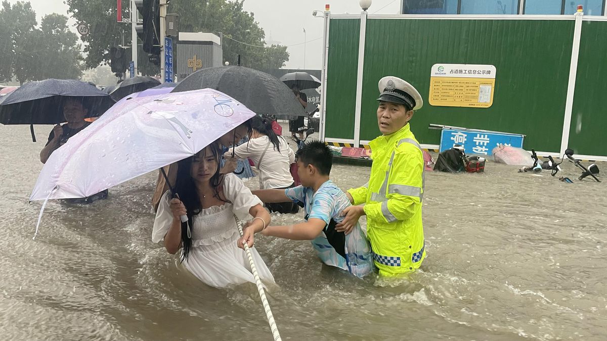Cảnh s&aacute;t hướng dẫn người d&acirc;n đi qua một đoạn đường ngập trong cơn mưa lớn tại Trịnh Ch&acirc;u ng&agrave;y 20/7 - Ảnh: AP