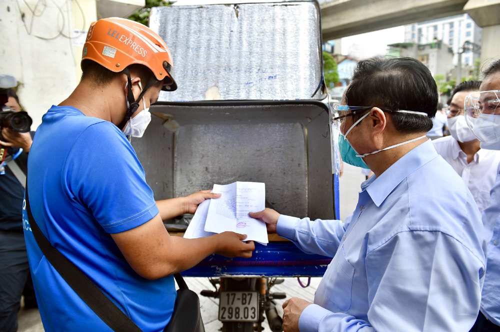 Thủ tướng Phạm Minh Ch&iacute;nh kiểm tra giấy ph&eacute;p đi đường v&agrave; khai b&aacute;o y tế của một nh&acirc;n vi&ecirc;n giao h&agrave;ng tr&ecirc;n địa b&agrave;n quận Thanh Xu&acirc;n.&nbsp;Ảnh: VGP.