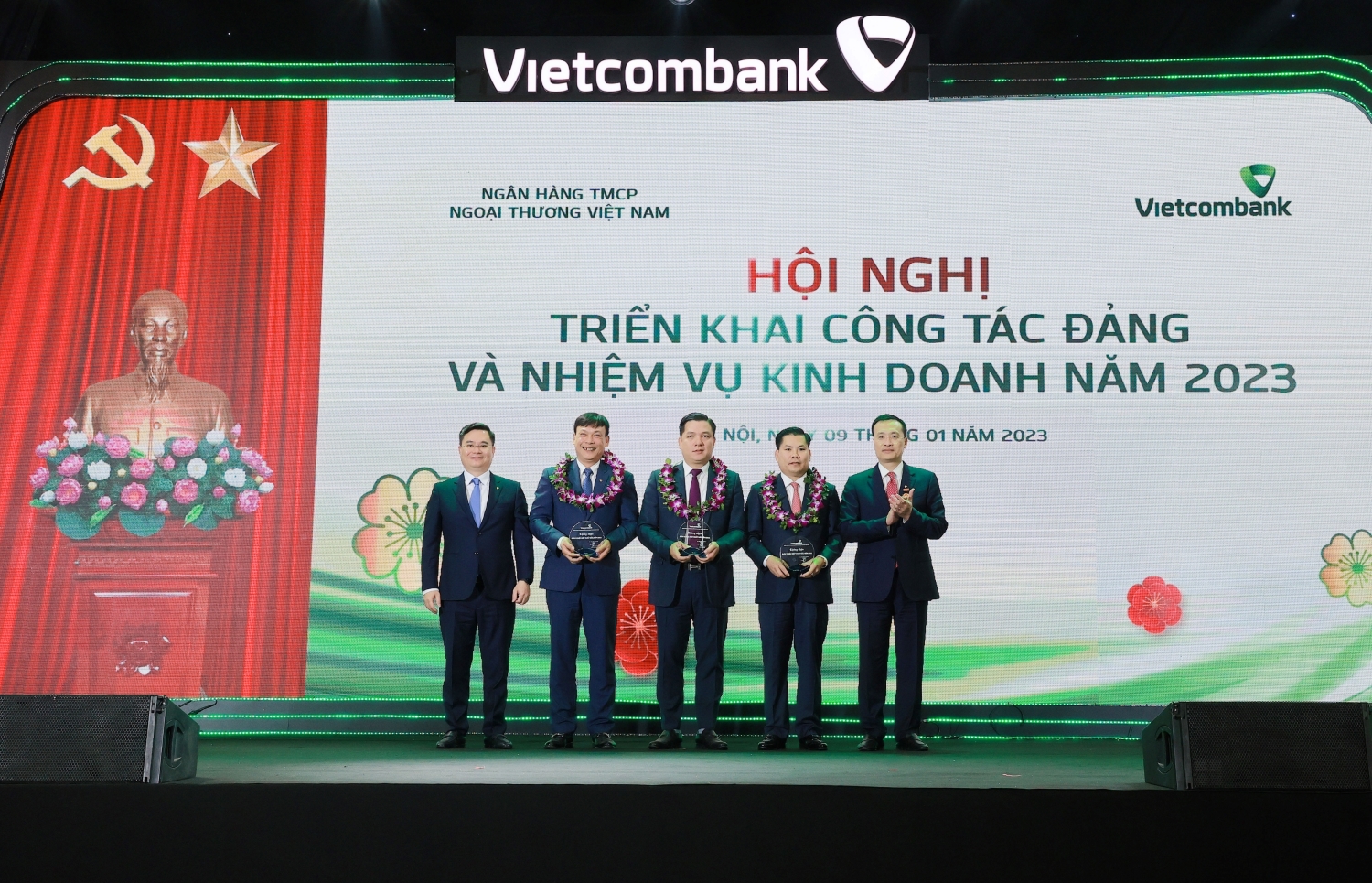 Đồng chí Phạm Quang Dũng - Ủy viên Ban Thường vụ Đảng ủy Khối DNTW, Bí Thư Đảng ủy, Chủ tịch HĐQT Vietcombank (ngoài cùng bên phải) và đồng chí Nguyễn Thanh Tùng - Phó Tổng Giám đốc phụ trách Ban điều hành (ngoài cùng bên trái) trao biểu trưng và tặng hoa cho 3 chi nhánh xuất sắc nhất hệ thống năm 2022 tại Hội nghị triển khai công tác Đảng và nhiệm vụ PG88 Uy Tín Số 1 Việt Nam năm 2023 diễn ra tại Hà Nội, ngày 9/1/2023.